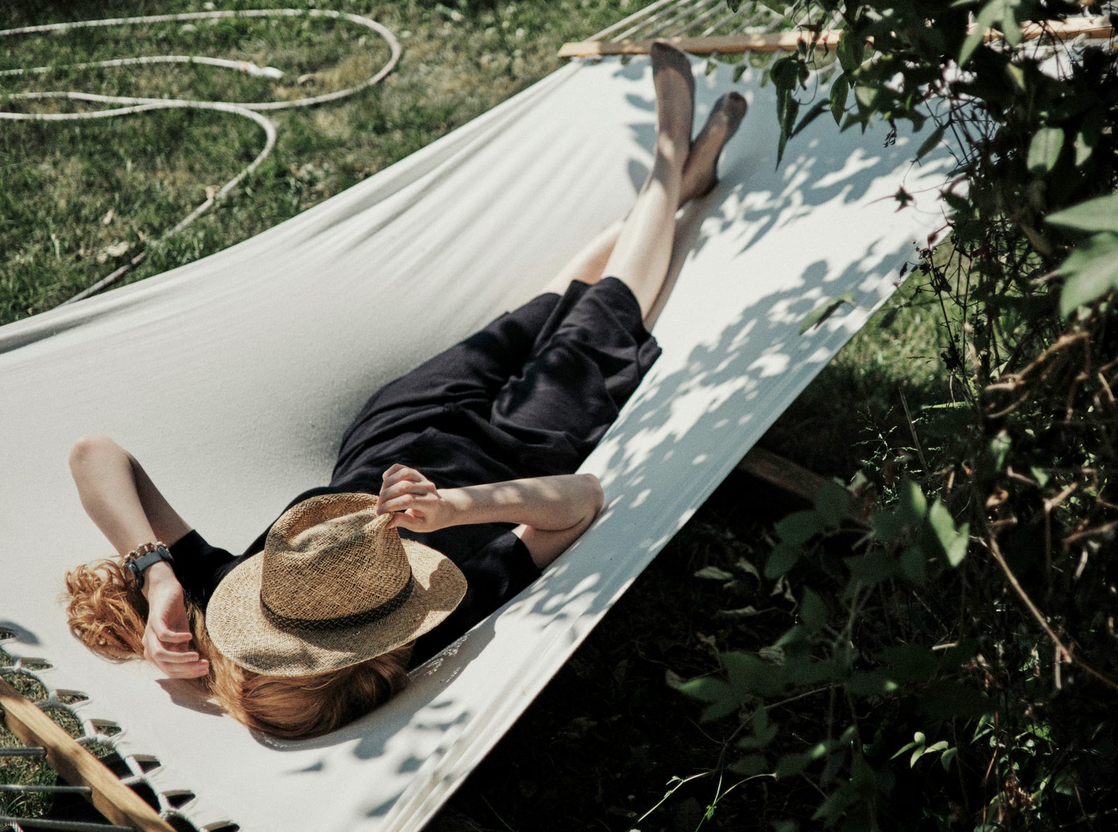Person resting in a hammock in dappled shade with a straw hat over their face